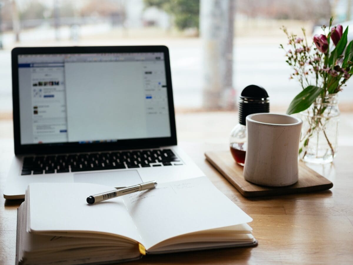 MacBook Pro near white open book and a coffee mug, a favourite of the creator